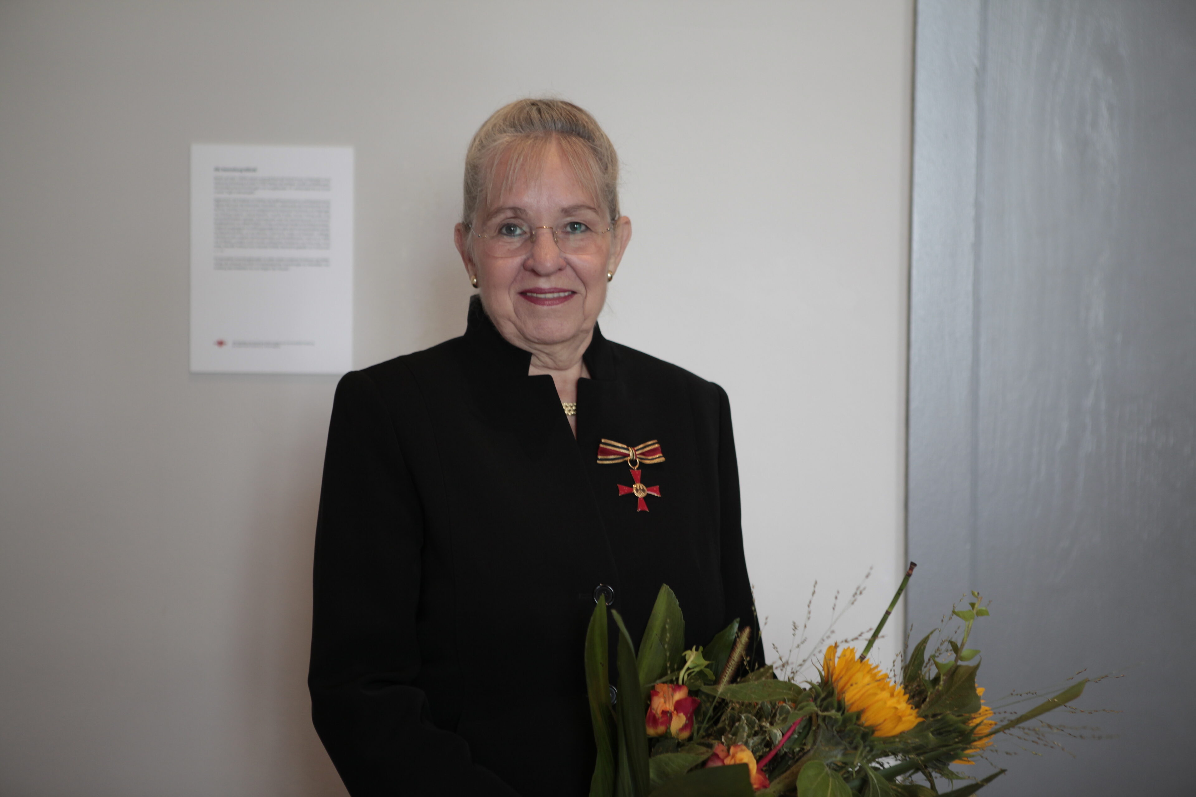 Dorothee Dickenberger steht vor einer Wand und hält einen Strauß Blumen in der Hand. 