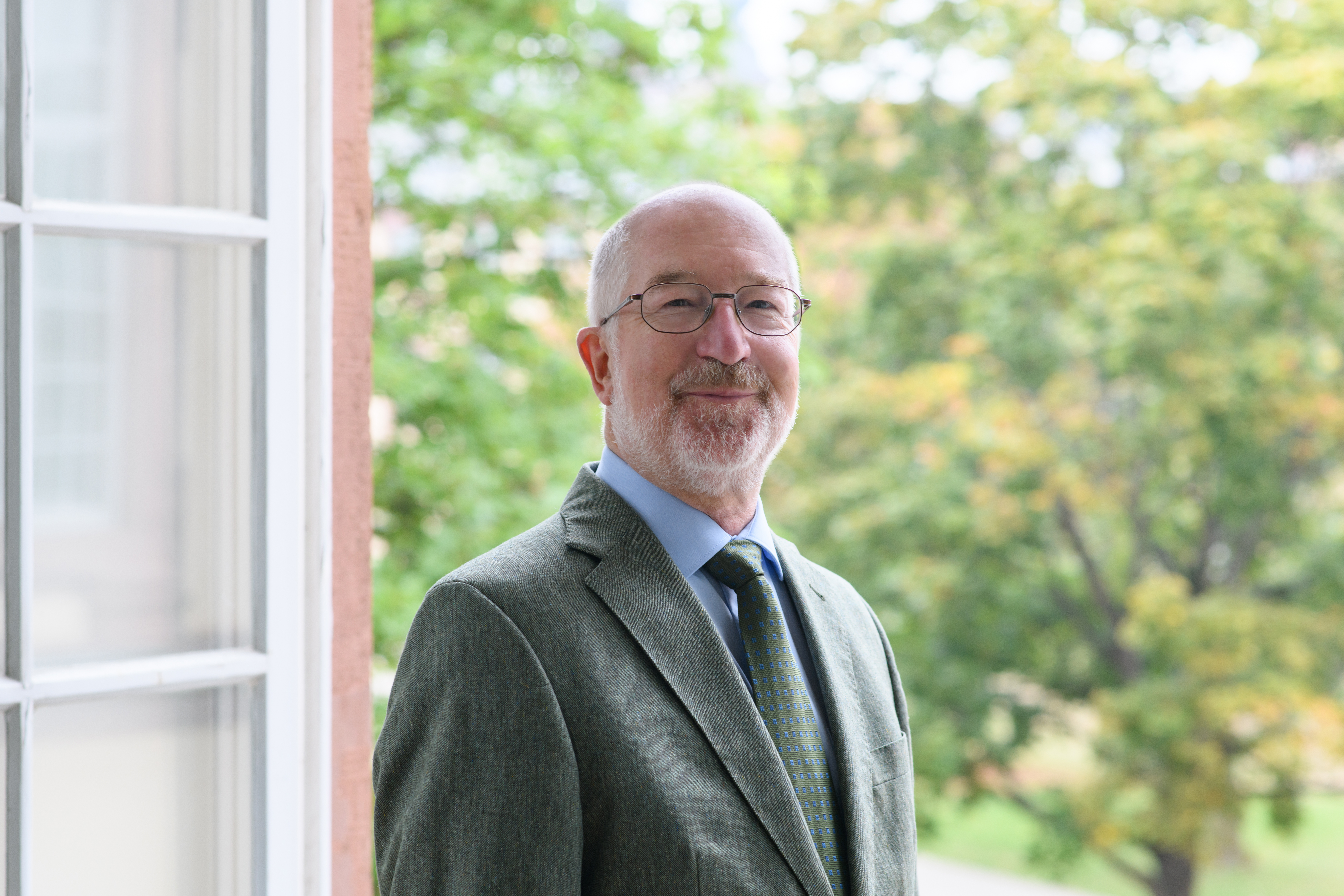 Portrait von Jochen Taupitz. Er trägt einen grünen Anzug und steht lächelnd vor einem Fenster.
