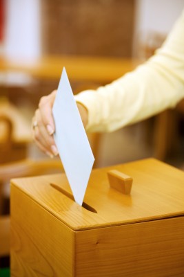 Eine Frau steckt einen weißen Briefumschlag in eine Wahlurne.