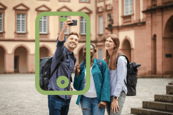 Drei Personen stehen auf dem Ehrenhof und machen ein Selfie. Darüber schwebt ein grünes Smartphone-Icon