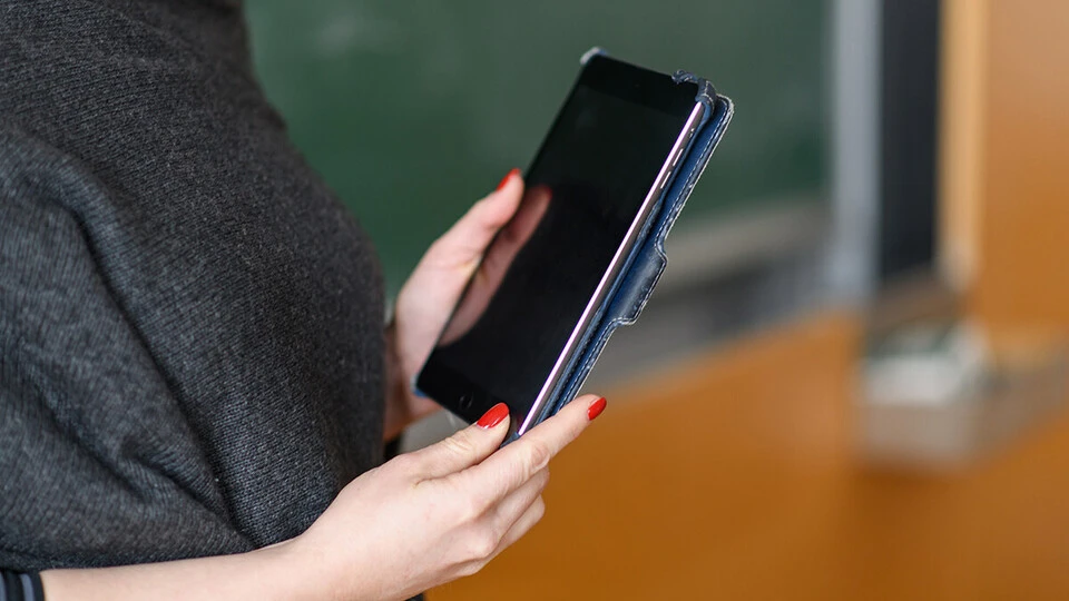 Seitenansicht auf eine Person, die ein IPad in den Händen hält. Das Gesicht oder der Körper abwärts der Hüfte sind nicht zu sehen.