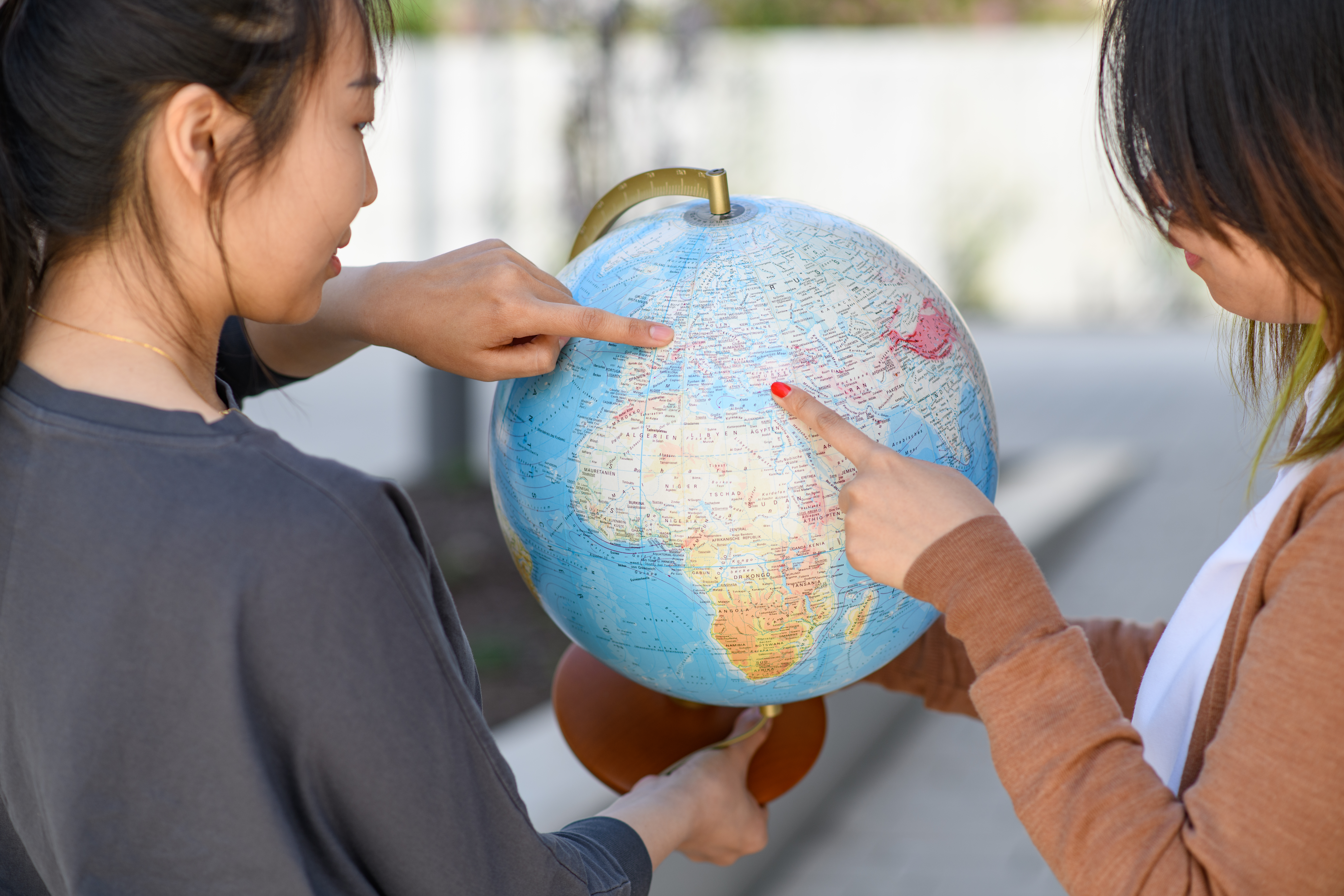 Zwei Studierende halten einen Globus in den Händen und deuten mit ihren Fingern darauf 