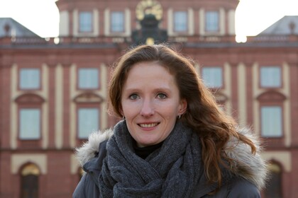 Prof. Hoisl hat lange braune Haare und steht vor dem Schloss.