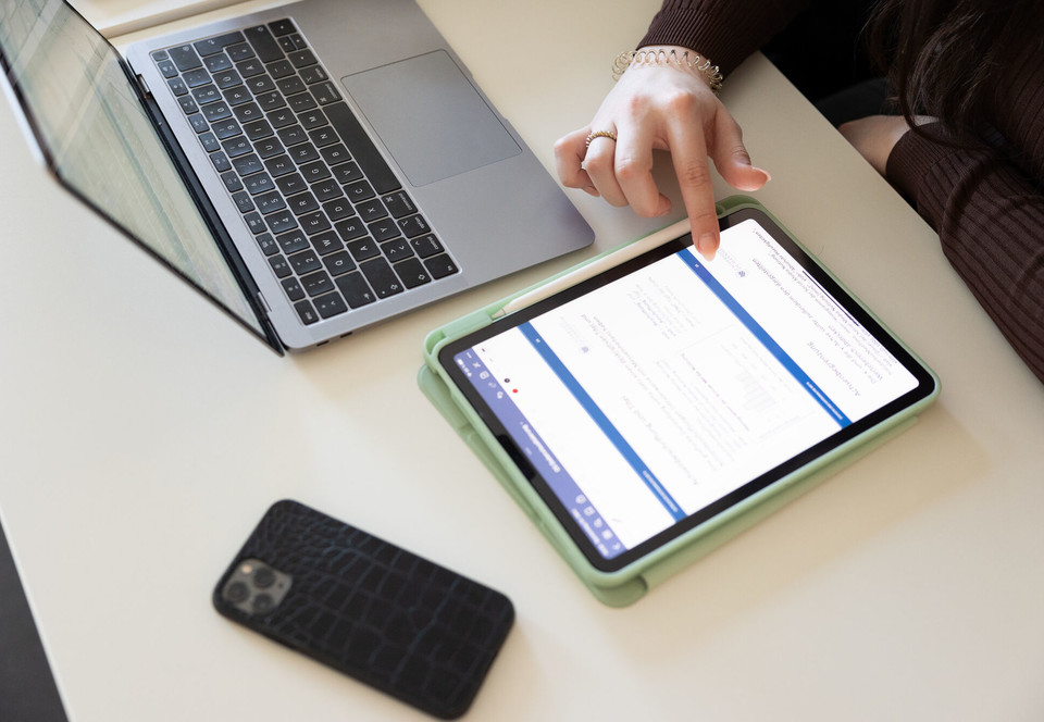 Digitales Lernen Eine Studentin tippt auf ihrem Tablet, ihr Handy und Laptop liegen daneben auf dem Tisch.