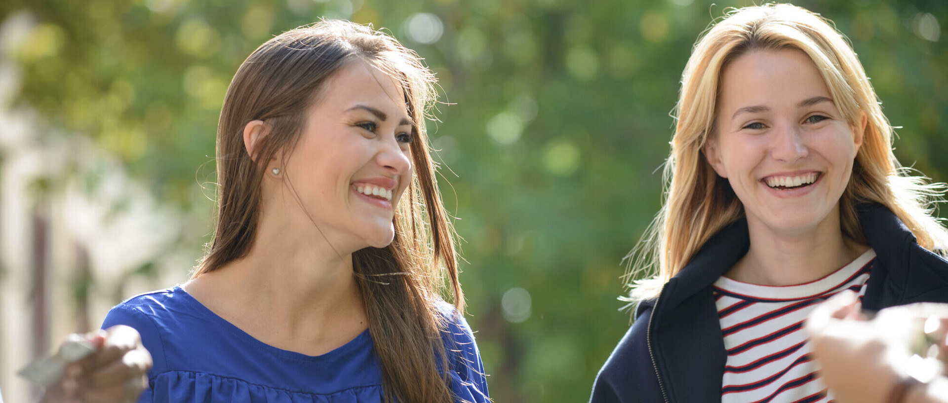 Zwei lachende Studentinnen vor einem grünen Hintergrund