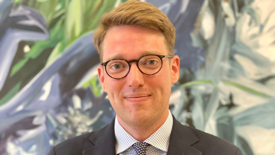 Prof. Vetter has short blond hair and wears glasses. He wears a suit and tie.