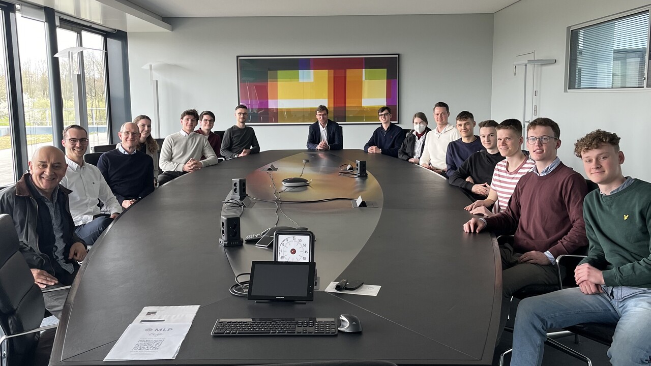 Personen sitzen um einen schwarzen Tisch herum auf dem Elektronik liegt.