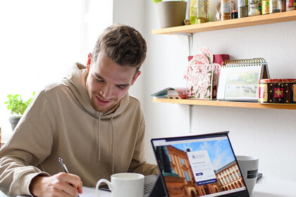 Zwei Personen sitzen sich am Tisch gegenüber. Auf dem Tisch sind Schreibmaterialien, ein Laptop und kaffeetassen