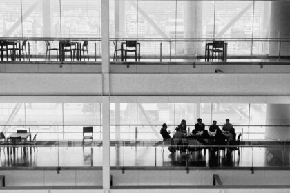 Schwarz-weißes Bild einer Vorstandssitzung in einem modernen Bürogebäude mit Glasfassade. Führungskräfte sitzen an einem Konferenztisch und symbolisieren unternehmerische Entscheidungsfindung und Corporate Governance.