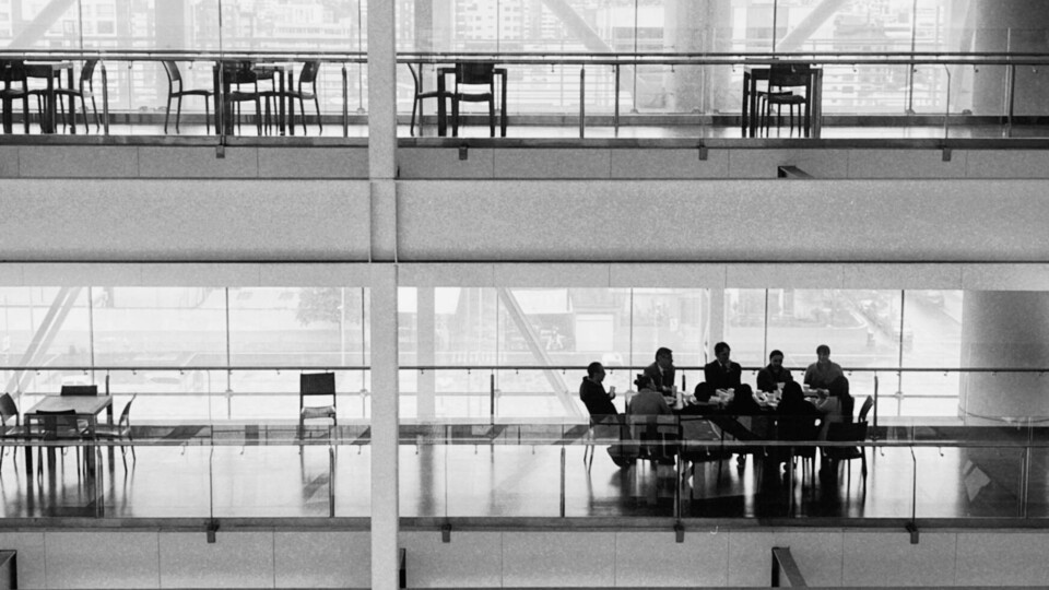 Black-and-white image of a corporate meeting in a modern glass office building, with executives seated around a conference table, symbolizing corporate decision-making and governance.