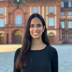 Raquel Oliveira has long brown hair and is wearing a dark top. The castle can be seen in the background.