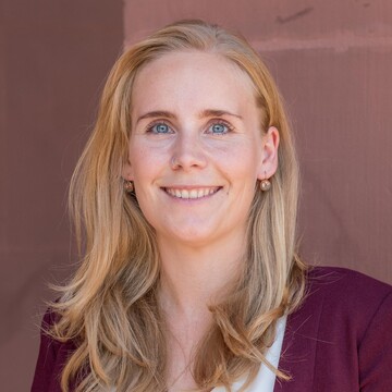 Kristin Schorb hat lange blonde Haare und trägt eine helle Bluse und eine rote Jacke.