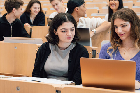 Junge Menschen sitzen im Vorlesungssaal. Einige haben Laptops vor sich.