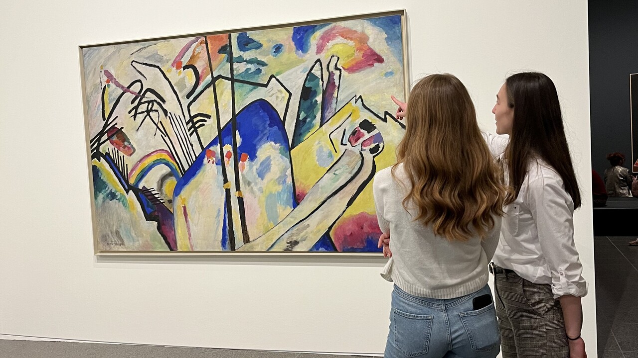 two people stand in front of a large picture hanging on a white wall