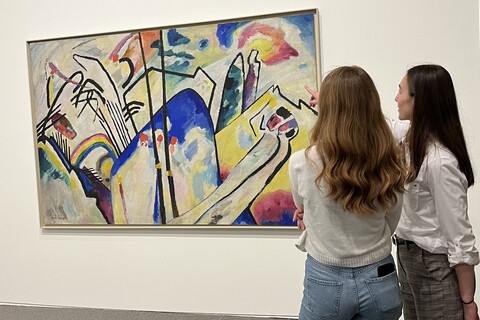 two people stand in front of a large picture hanging on a white wall