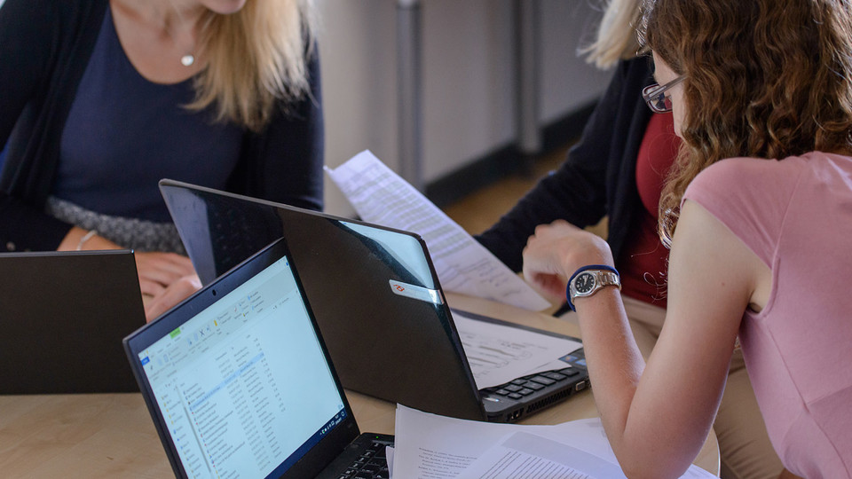 Drei Studentinnen sitzen mit ihren Laptops an einem Tisch und lernen gemeinsam.