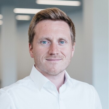 Roland Kassenmeier hat kurze blonde Haare. Er trägt ein weißes Hemd und lächelt in die Kamera