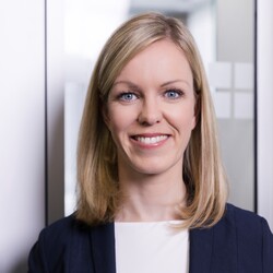 Britta Alisa Layendecker hat schulterlange blonde Haare und trägt ein weißes Oberteil und einen dunklen Blazer.