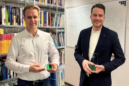 Prof. Stahl steht vor einem Bücherregal und hält einen Preis. Er hat kurze blonde Haare und trägt ein weißes Hemd. Prof. Glenk steht vor einem Whiteboard und hält einen Preis. Er hat kurze braune Haare und trägt ein Jackett