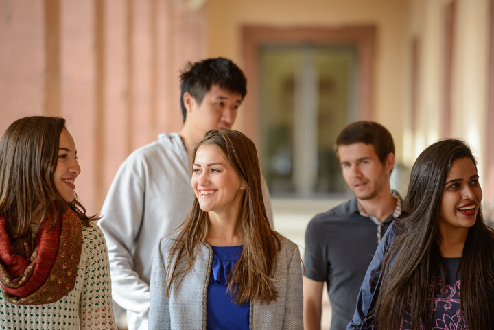 Internationale Studierende Fünf Studierende, die durch die Arkaden im Ehrenhof spazieren und sich lebhaft unterhalten.