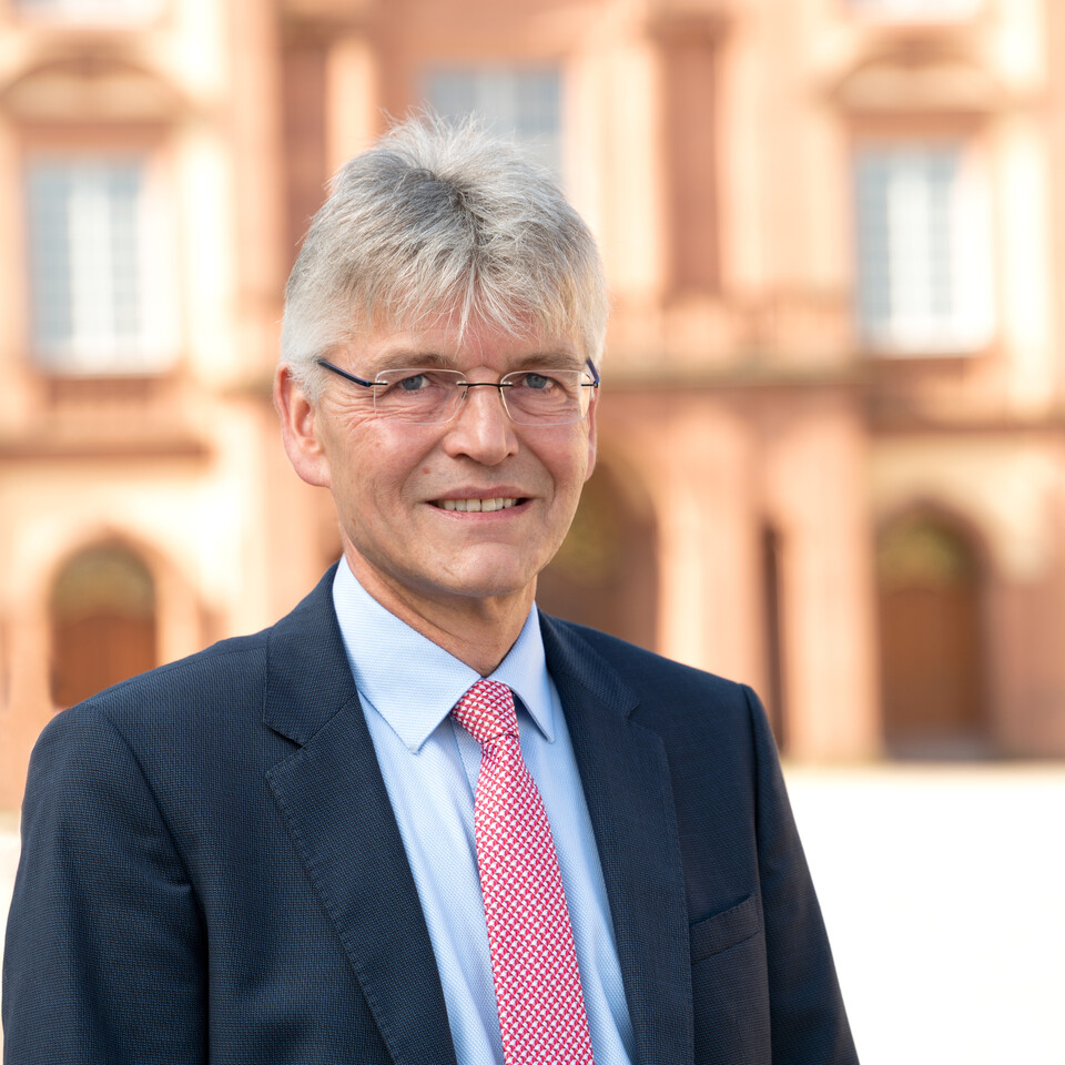 Prof. Spengel hat kurze Haare und trägt eine Brille sowie einen blauen Anzug und eine rosa Krawatte