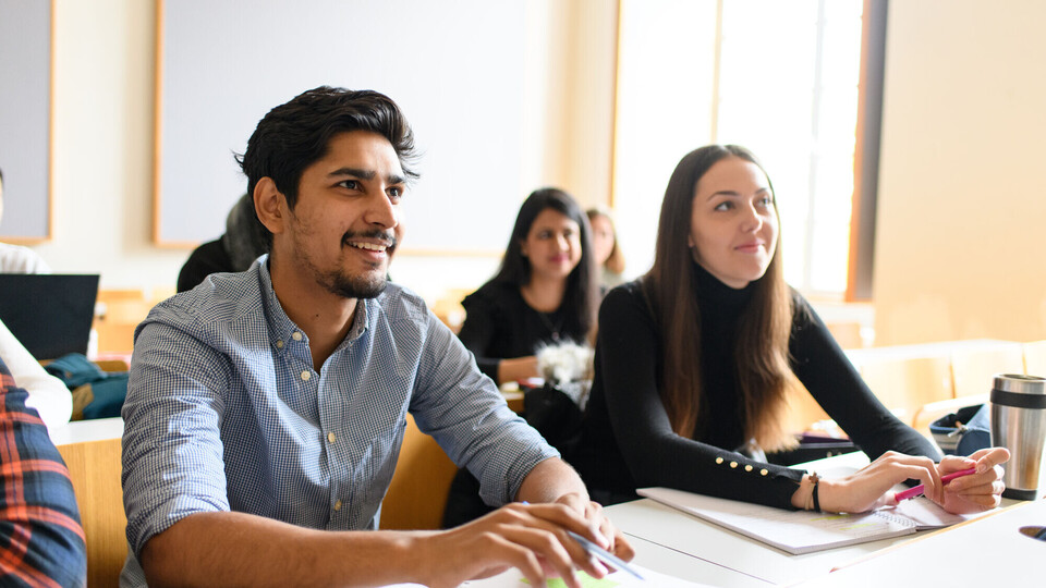 Eine Studentin und ein Student hören begeistert bei einem Vortrag zu.