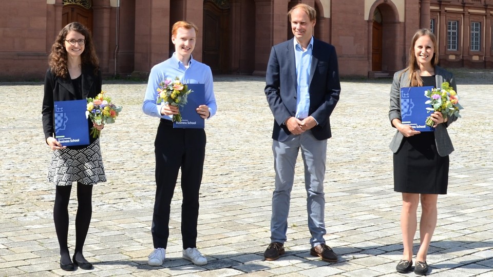 vier Personen stehen im Ehrenhof. Drei haben Blumen und Urkunden in der Hand