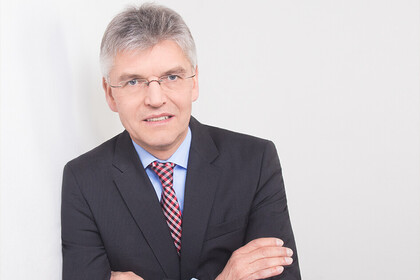 Christoph Spengel hat kurze graue Haare und eine schmlae randlose Brill. Er trägt ein helblaues Hemd, eine rote Krawatte und ein dunkelgraues Jackett.
