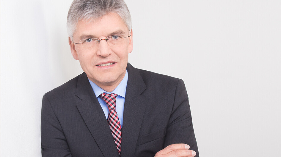 Christoph Spengel hat kurze graue Haare und eine schmlae randlose Brill. Er trägt ein helblaues Hemd, eine rote Krawatte und ein dunkelgraues Jackett.