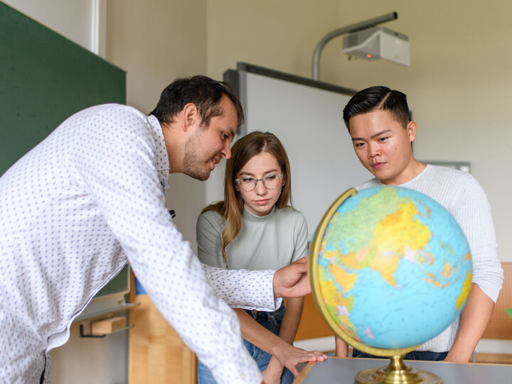 Ein Lehrer und drei Studierende um einen Globus herum in einem Klassenzimmer