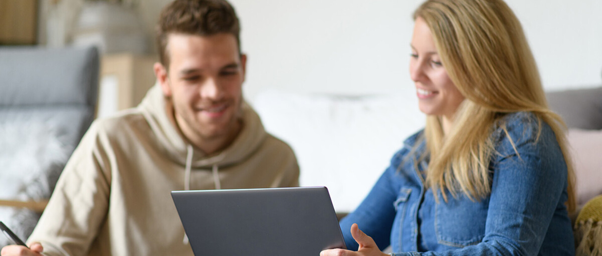 Eine junge Frau zeigt einem jungen Mann etwas auf dem Laptop.