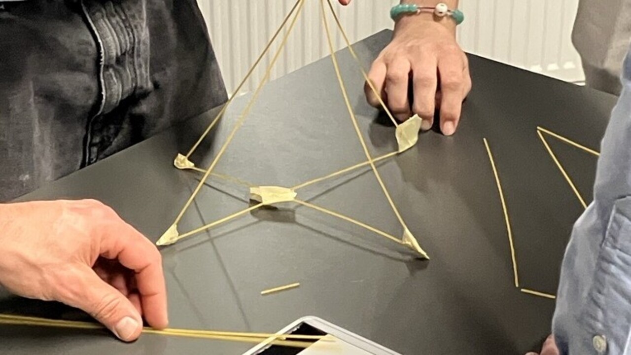 Hände, die ein Kontrukt aus langen Stäben auf einem Tisch bauen.