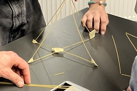 Hände, die ein Kontrukt aus langen Stäben auf einem Tisch bauen.