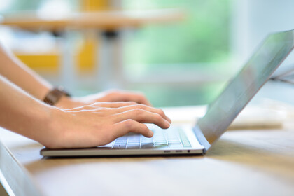 Eine Person tippt auf einem silbernen Laptop.