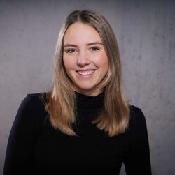 Hannah Balke has long blonde hair and is wearing a black turtleneck sweater. The background is gray.