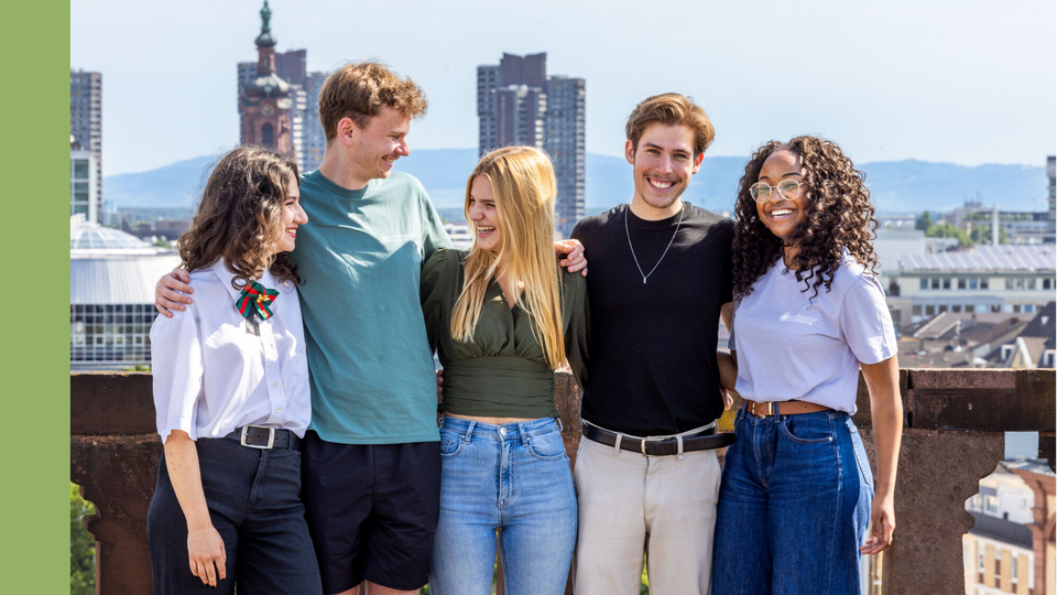 Fünf Studierende stehen auf dem Dach des Barockschlosses für ein Gruppenfoto. Im Hintergrund ist die Stadt Mannheim zu sehen.