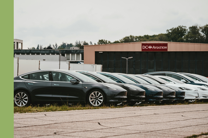 Mehrere Elektroautos stehen aufgereiht auf einem Parkplatz vor einem Hangar.
