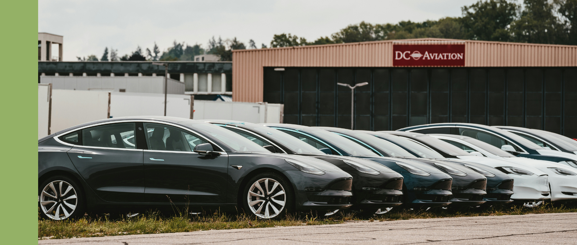 Mehrere Elektroautos stehen aufgereiht auf einem Parkplatz vor einem Hangar.