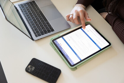 Digitales Lernen Eine Studentin tippt auf ihrem Tablet, ihr Handy und Laptop liegen daneben auf dem Tisch.