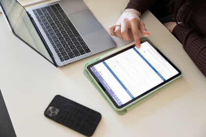 Eine Studentin tippt auf ihrem Tablet, ihr Handy und Laptop liegen daneben auf dem Tisch.