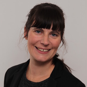 Frau mit langen braunen Haaren und schwarzer Bluse mit schwarzem Blazer