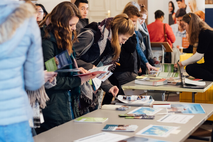 Mehrere Studieninteressierte, die beim Studieninfotag das Informationsmaterial auf Tischen sichten