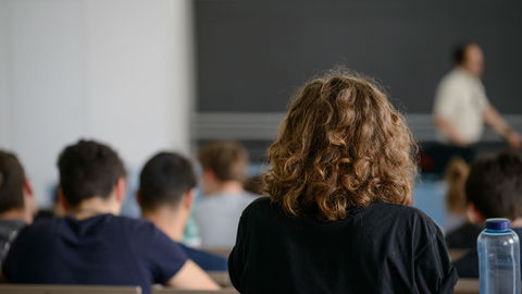 Studierende sitzen hintereinander in einem Hörsaal und hören bei einer Vorlesung zu.