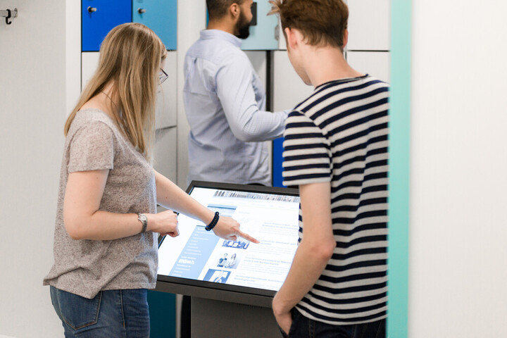 Studierende stehen an großem Touscreen
