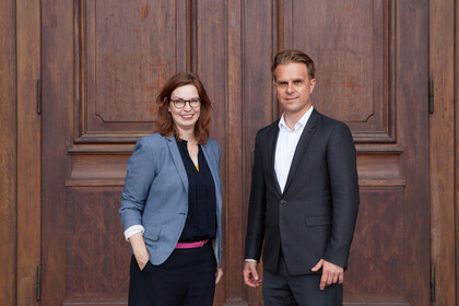 Florian Stahl und Sabine Gehrlein stehen vor einer großen Holztür. 