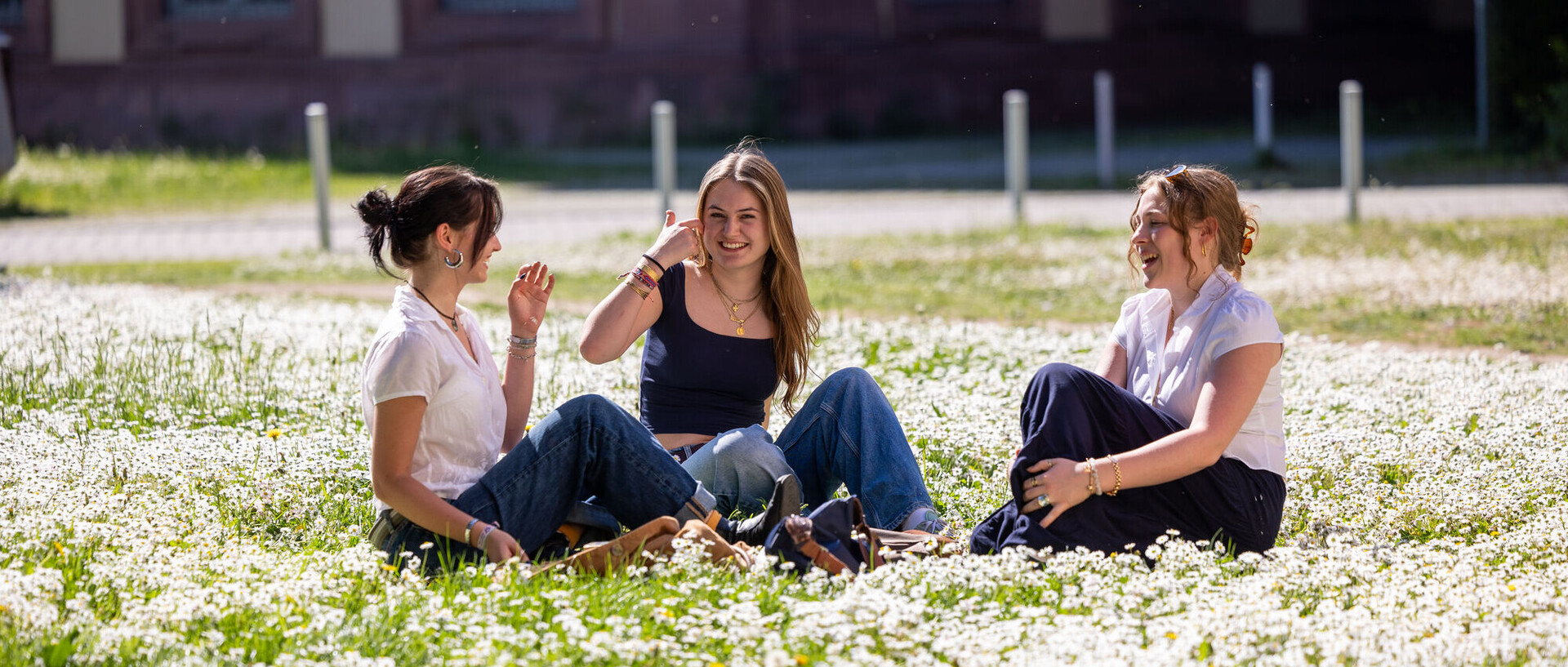 Drei weiblich gelesene Studierende sitzen auf der Neckarwiese und unterhalten sich.