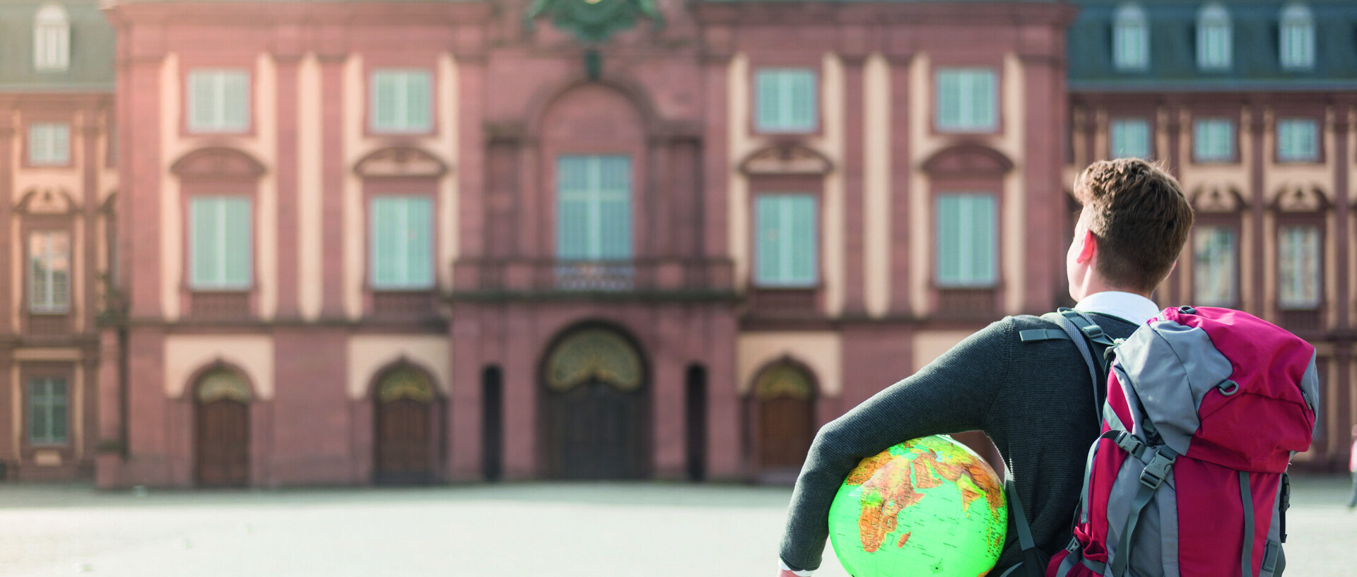 Student mit Weltkugel unterm Arm vorm Schloss von hinten