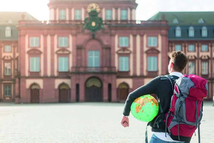 Student mit Weltkugel unterm Arm vorm Schloss von hinten
