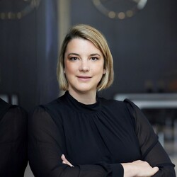 Katrin Lehmann hat kinnlange blonde Haare, trägt ein schwarzes Oberteil und hat die Arme vor der Brust verschränkt.
