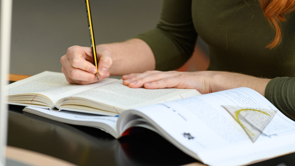 Studierende in der A3-Bibliothek Eine Frau macht sich in einem Buch Notizen.